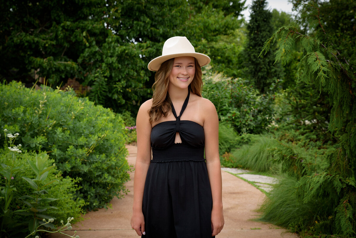 Luxemburg Casco High School senior girl wearing a long black dress and tan hat walking through flower gardens at the Green Bay Botanical Gardens in Green Bay, Wisconsin