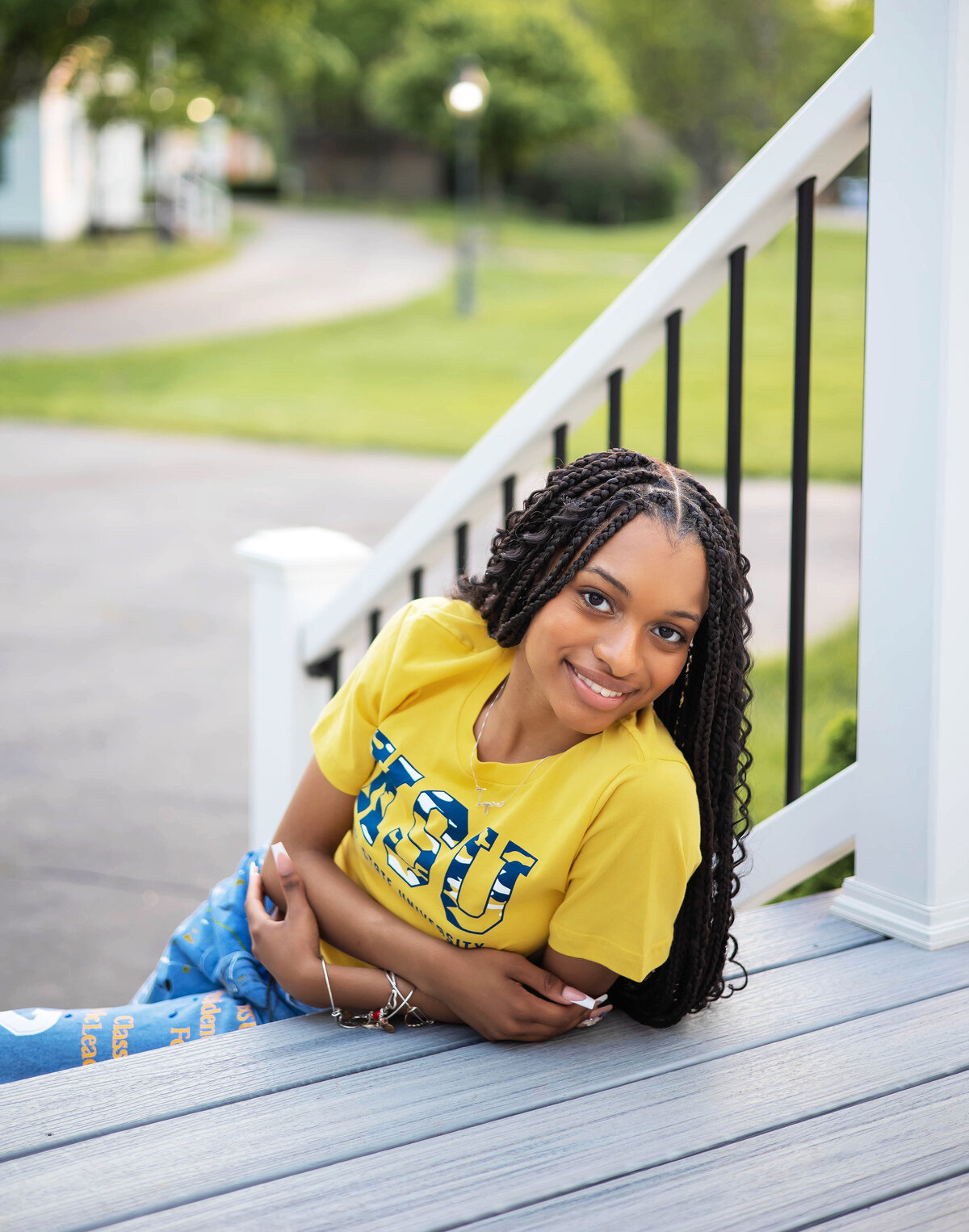 Taylor Heritage Park Senior Photoshoot | Taylor Michigan Senior Photographer, African American senior girl wearing yellow Kent State University t-shirt, decorated jeans, and gray and white Nikes laying on a step