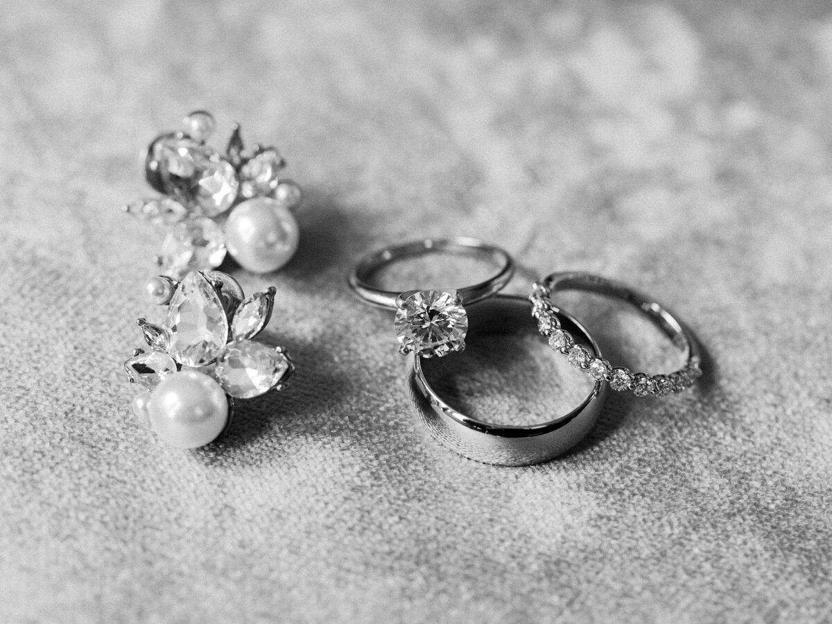 A closeup of bridal jewelry including earrings and wedding rings.