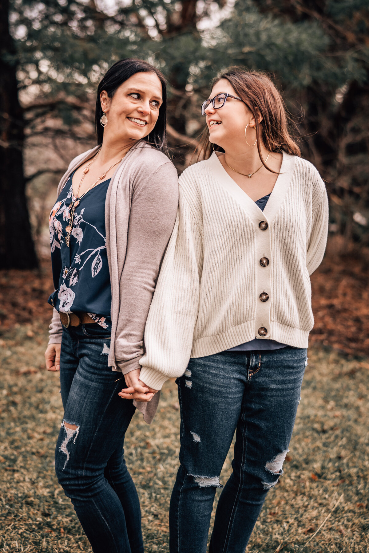 An image of a mom and her younger daughter holding hands back to back in their backyard.