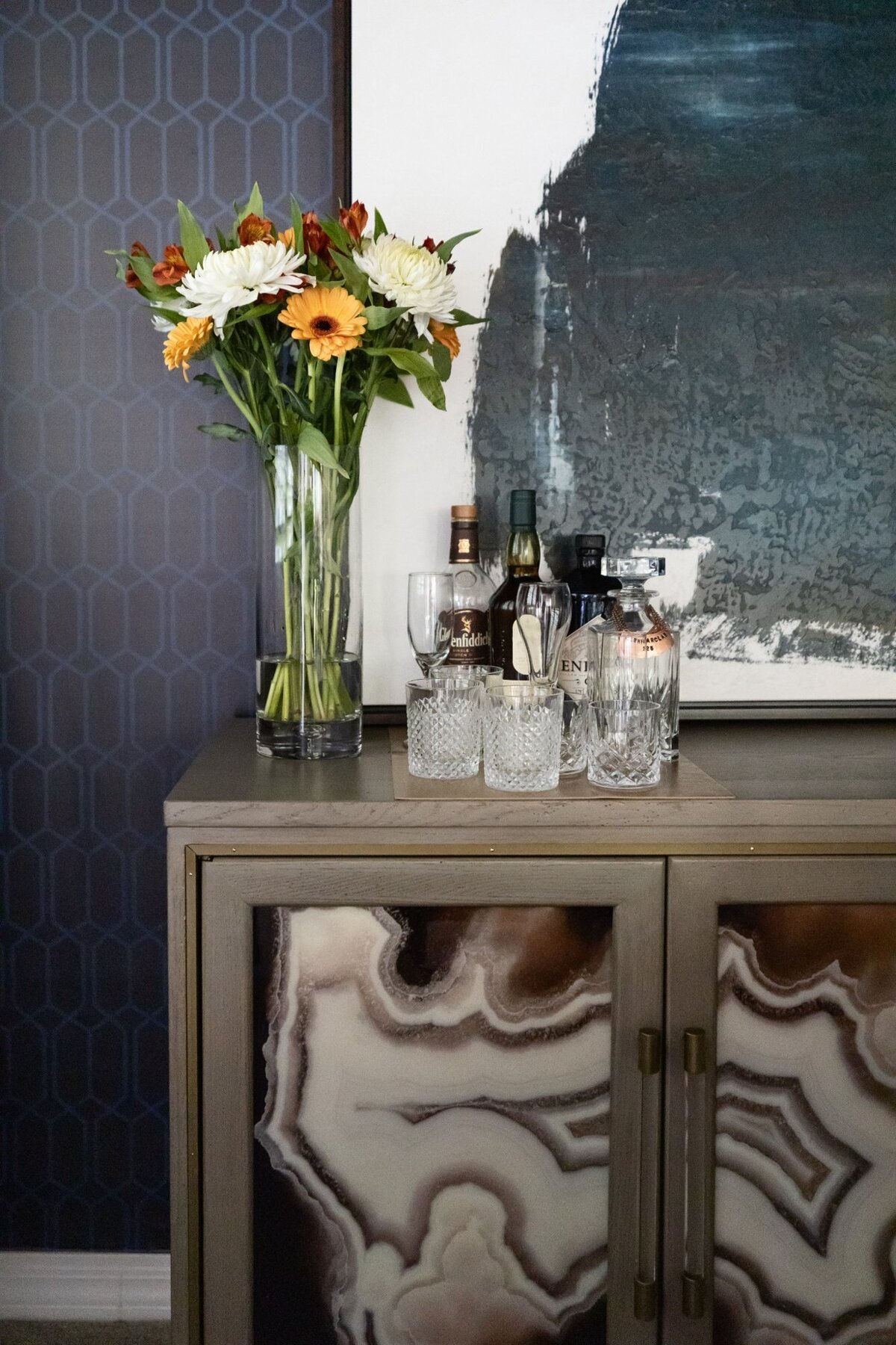 Elegant home bar corner with floral arrangement, textured wallpaper, and lounge chair in a Scottsdale residence.
