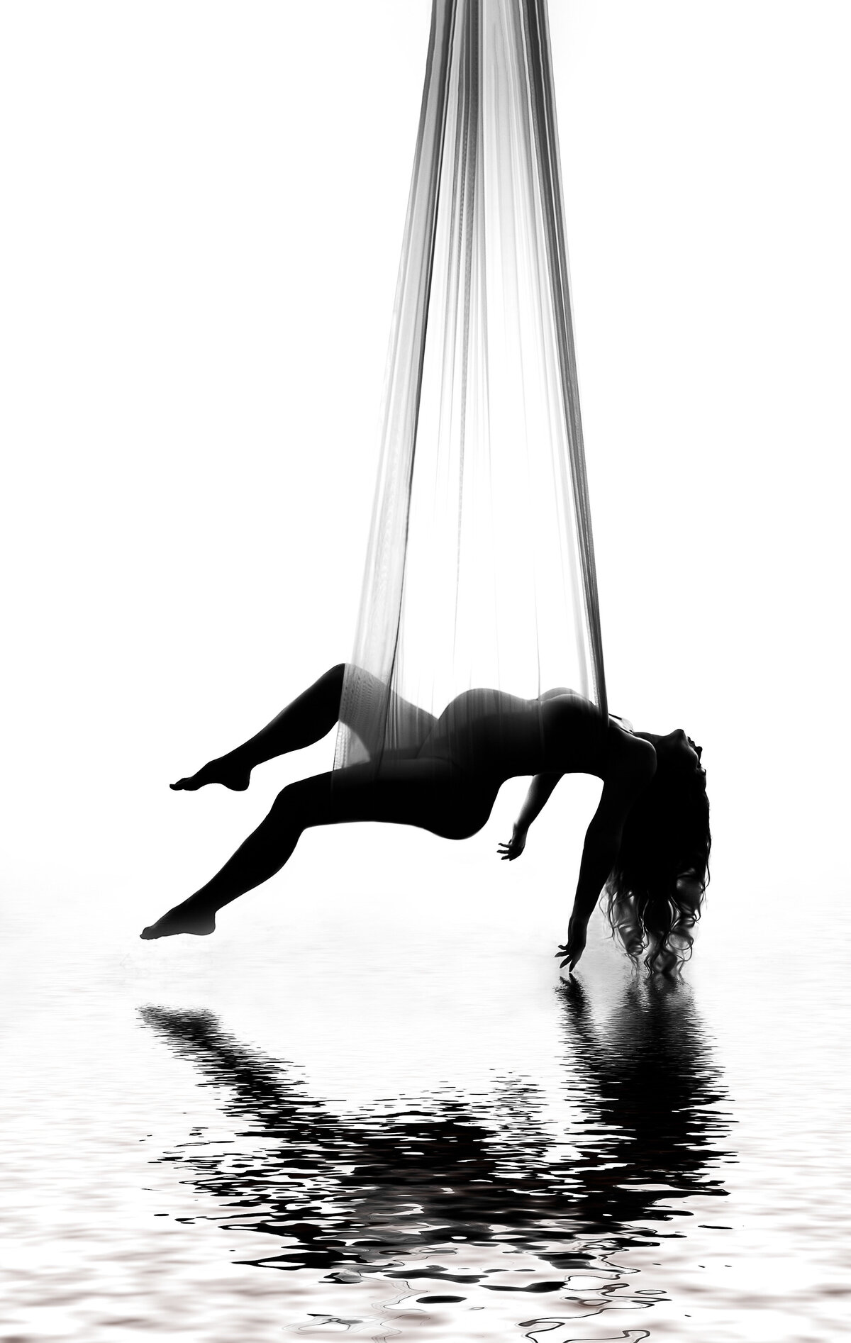 Expectant mom suspended with silks is posed bare. Her head and arms drape behind her and her back leg is raised above a reflective water pool. Captured by Bryn Mwar Philadelphia and Main Line photographer Liza Nicole.