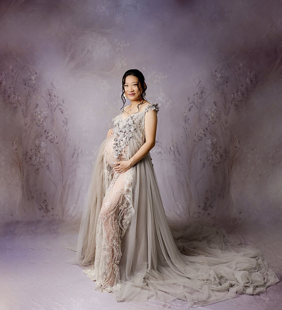 mom in grey dress holding pregnant belly on  purple backdrop