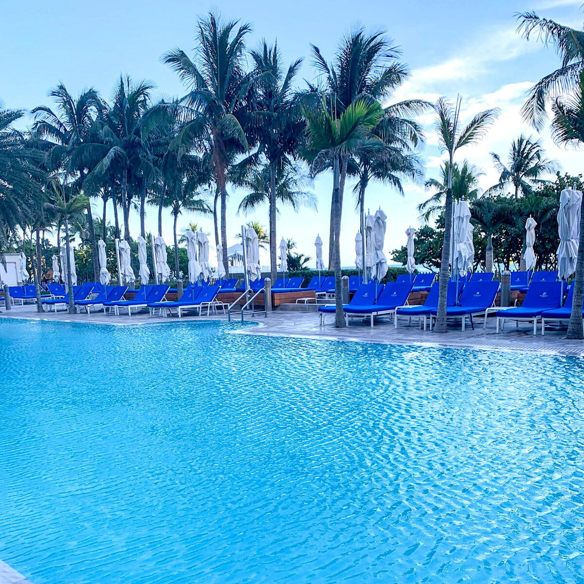  Luxurious beachfront pool surrounded by palm trees and blue cabanas at the St. Regis Bal Harbour, steps from PH-888