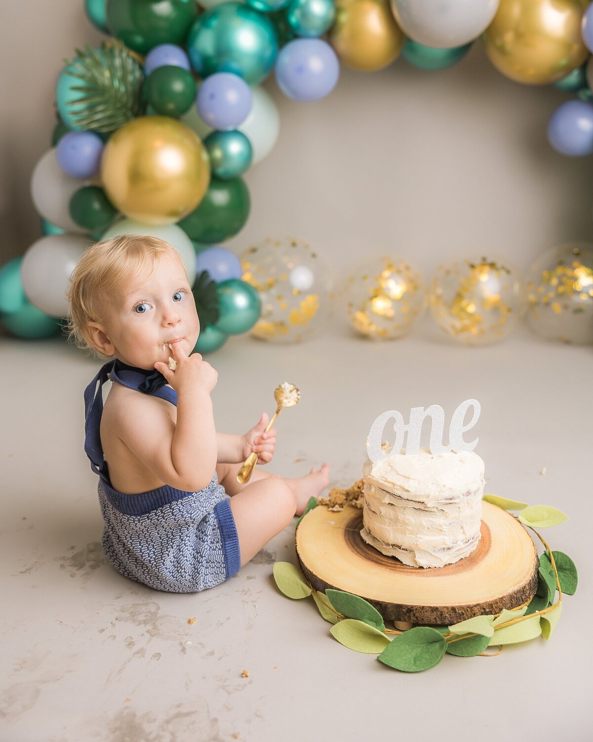 baby boy in blue overalls turning around eating cake in portland baby photography session by Ann Marshall