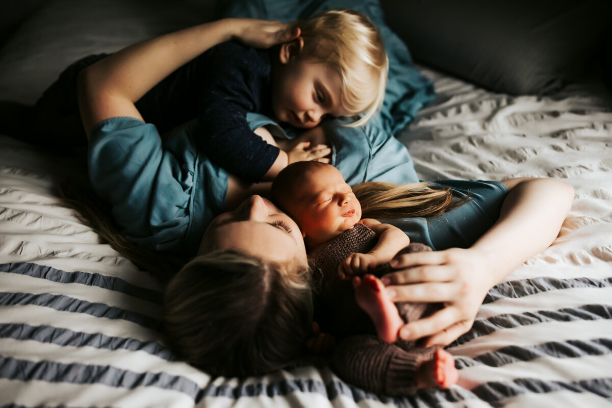 a mom cuddling with her newborn baby and toddler son in bed