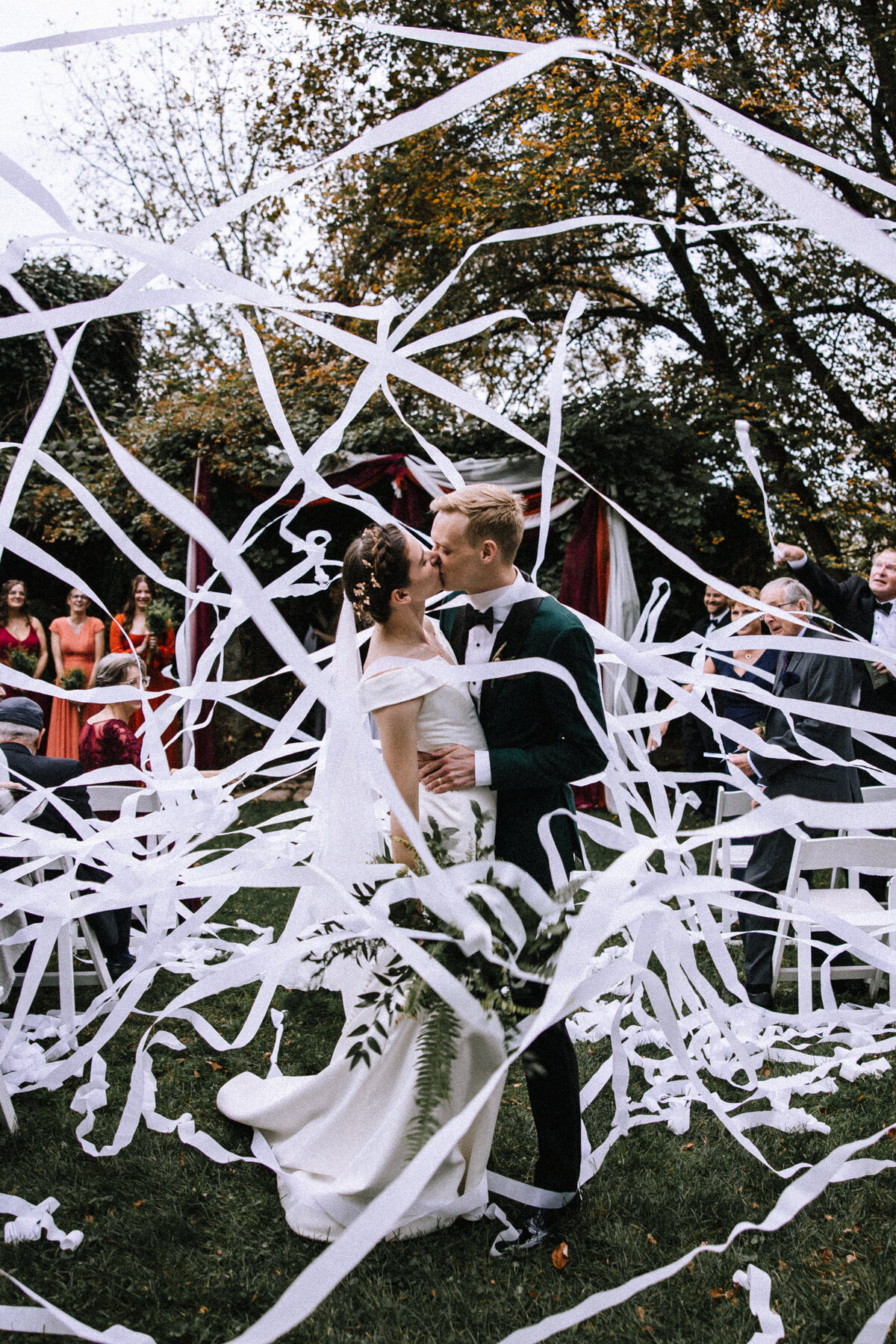 Bride and groom kissing at the end of the aisle with streamers flying around them. 