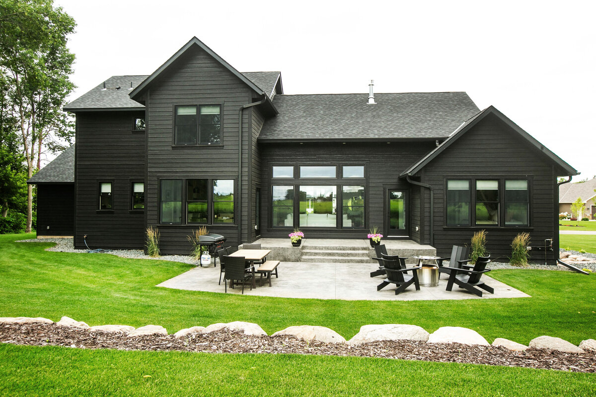 Exterior view of custom home in Otsego, Minnesota with black siding, large patio and windows built by Cornerstone Custom Builds