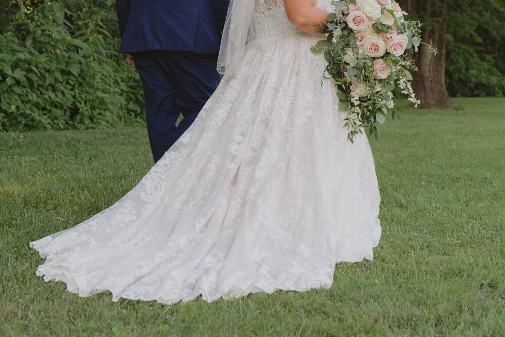 A photo of a bride and groom walking together through a grassy field next to woods at Hidden Meadows in Afton, TN. 