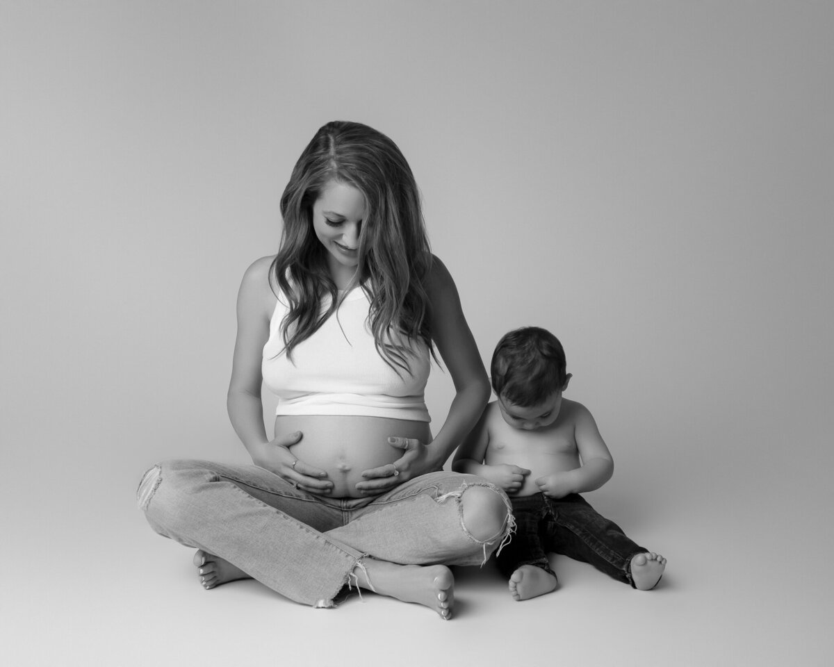 Sweet black and white maternity image of a mom with her toddler, capturing a playful moment between siblings-to-be.