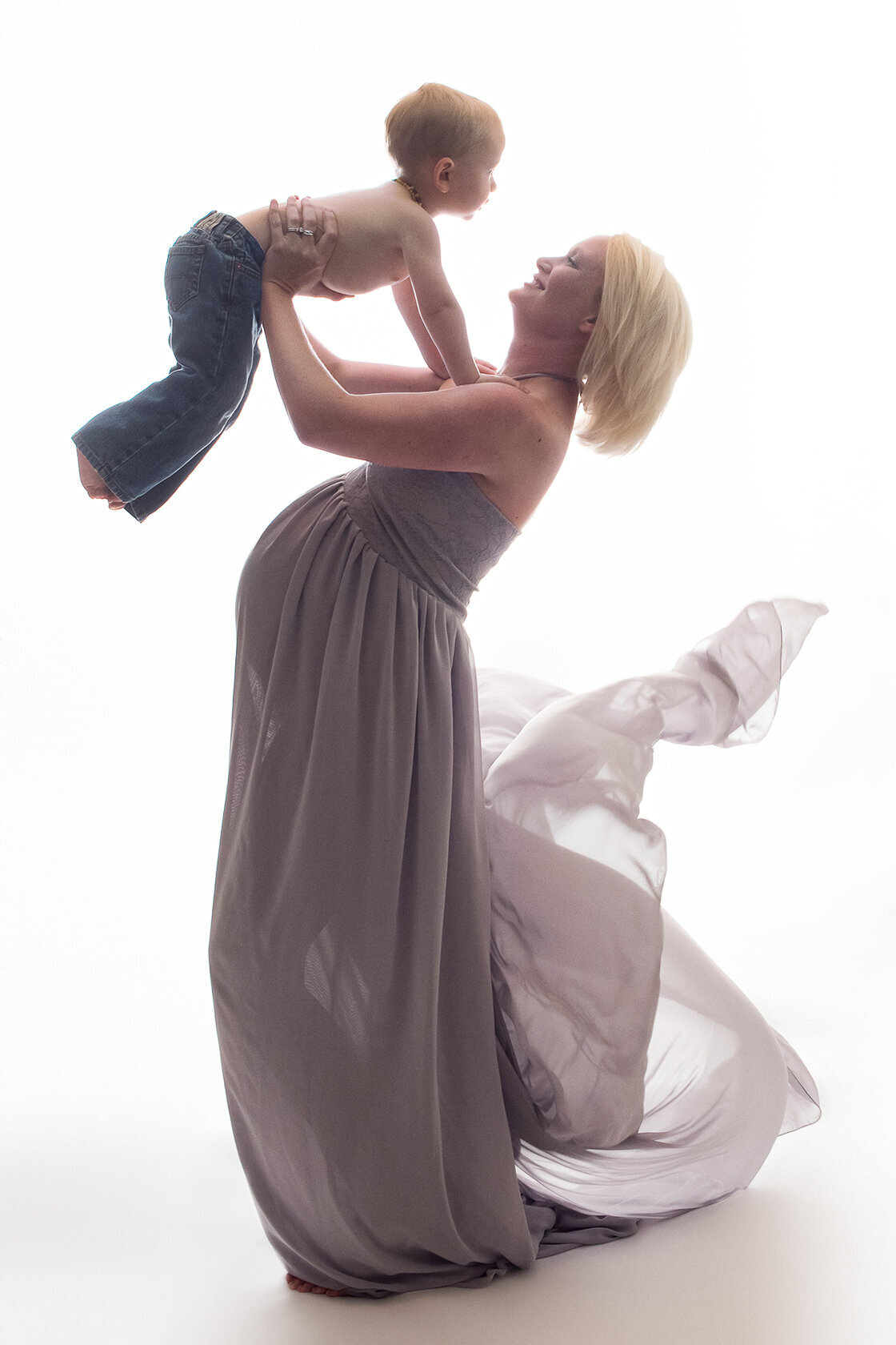 Blond pregnant woman hold up her toddler in this maternity portrait