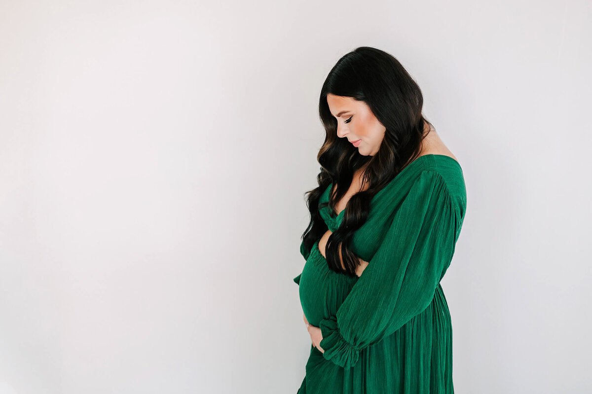 pregnant mom in green dress looking down praying over baby bump in Branson MO