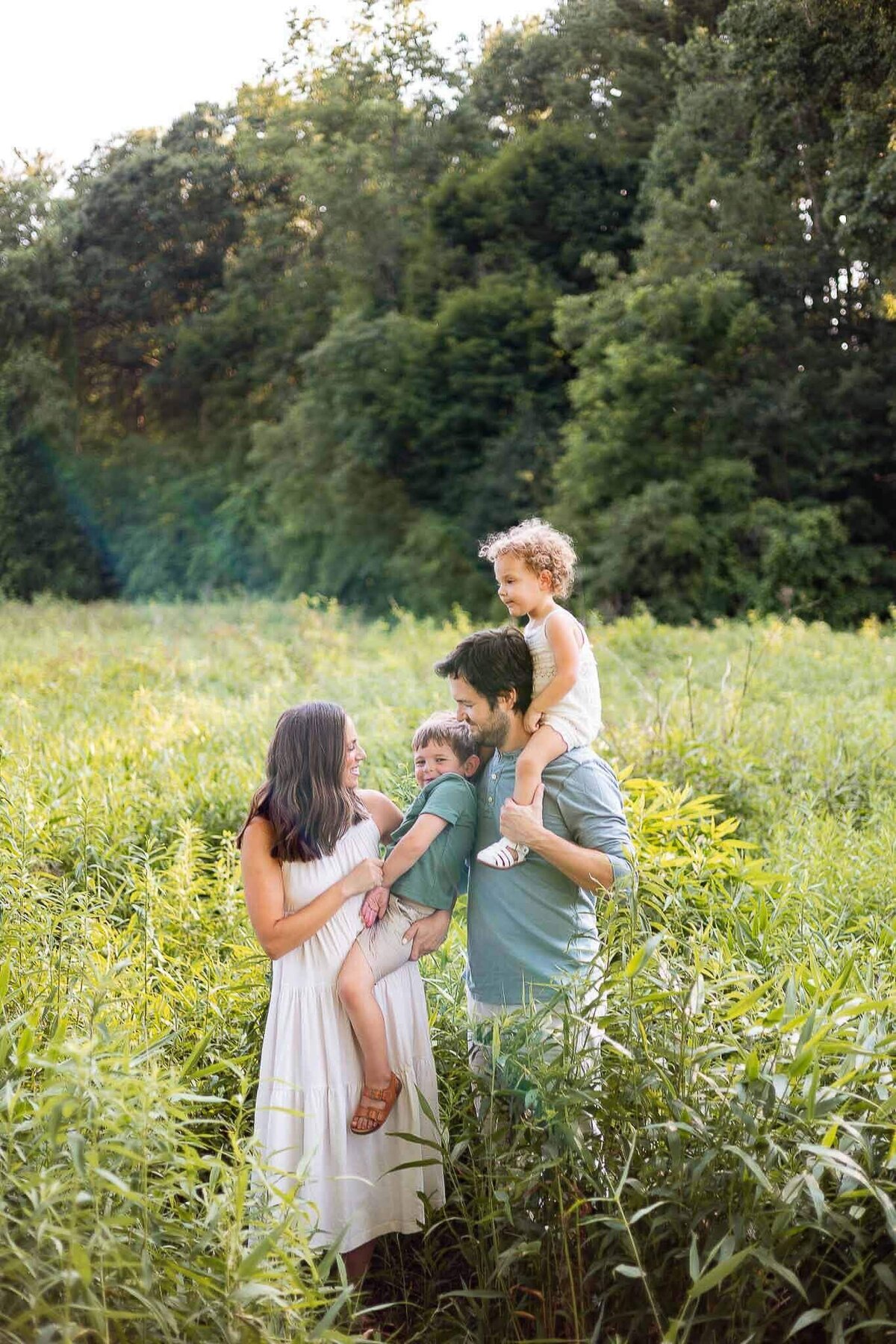 Family of four embracing in Cleveland Metropark field during summer family photography session.