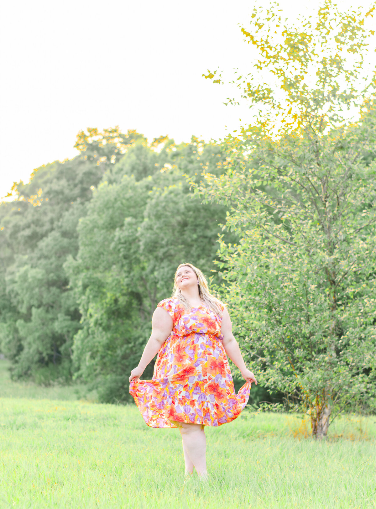 a woman twirls her skirt in a field with the sun setting behind her