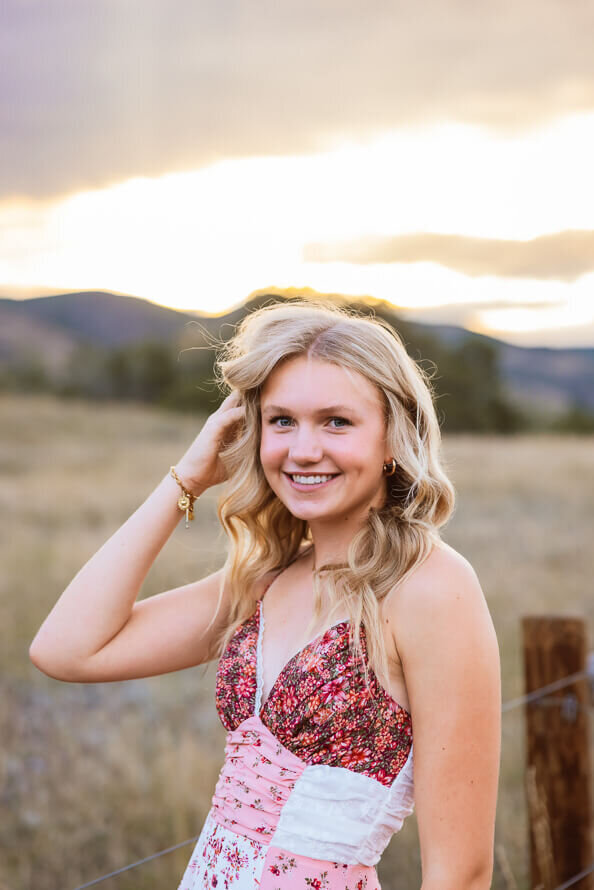Girl puts hair behind ear with sun setting behind her.