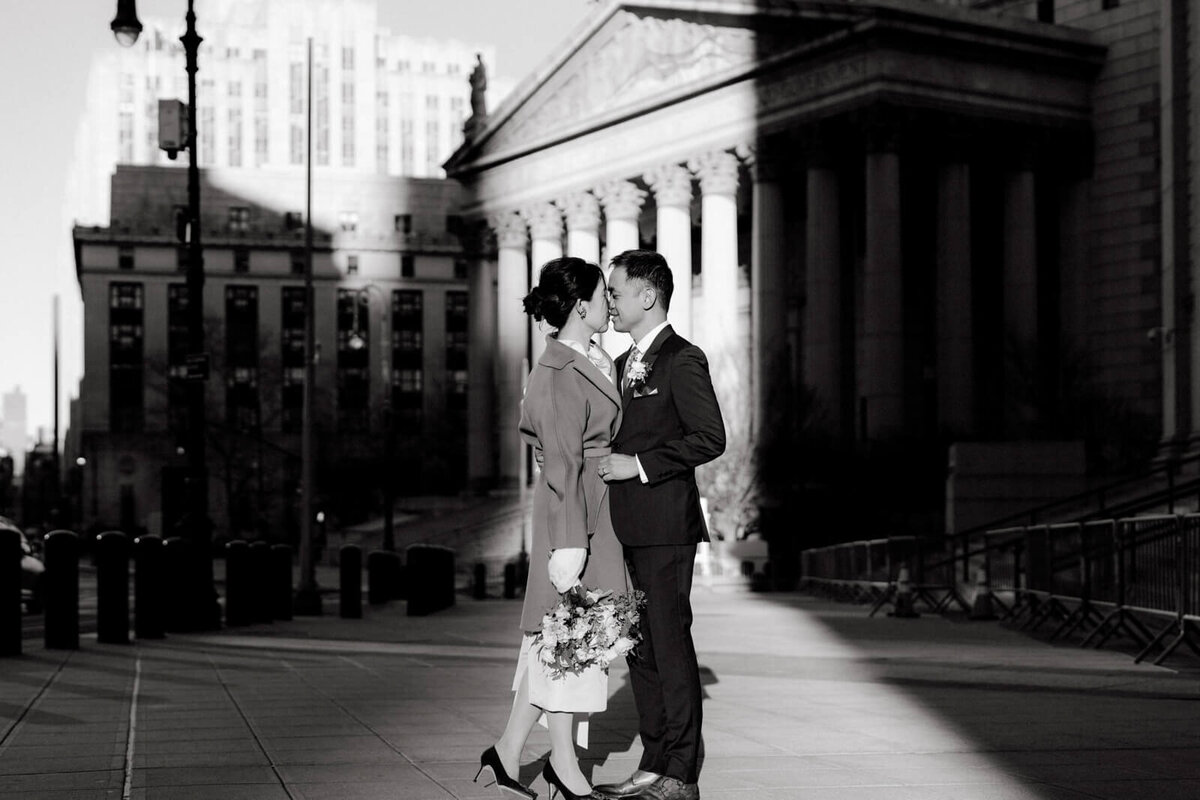 Black and white photo of the bride and groom kissing in front of an old building with columns.