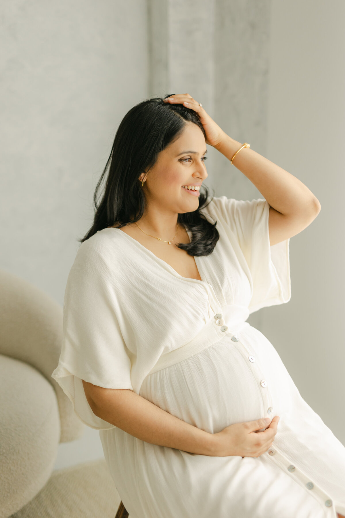 An expecting mom is smiling and looking out the window while loving her baby bump in a Toronto maternity session