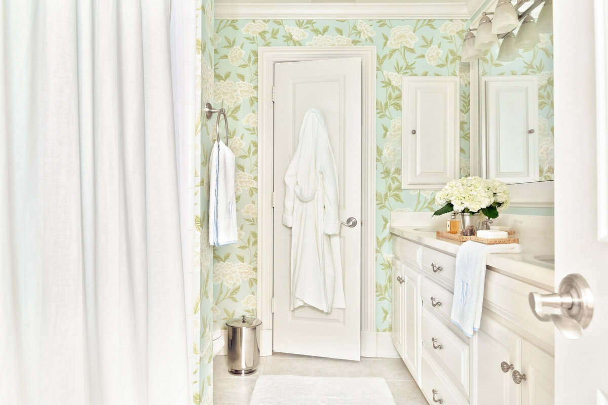 Fresh and timeless bathroom design with floral wallpaper, waite vanity, and embroidered bath towels.