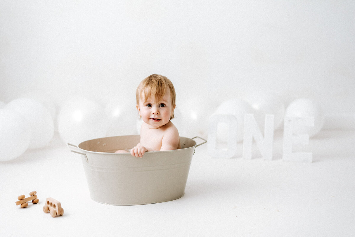 one year old girl in a small bath tub with wooden toys at billingshurst cake smash photoshoot