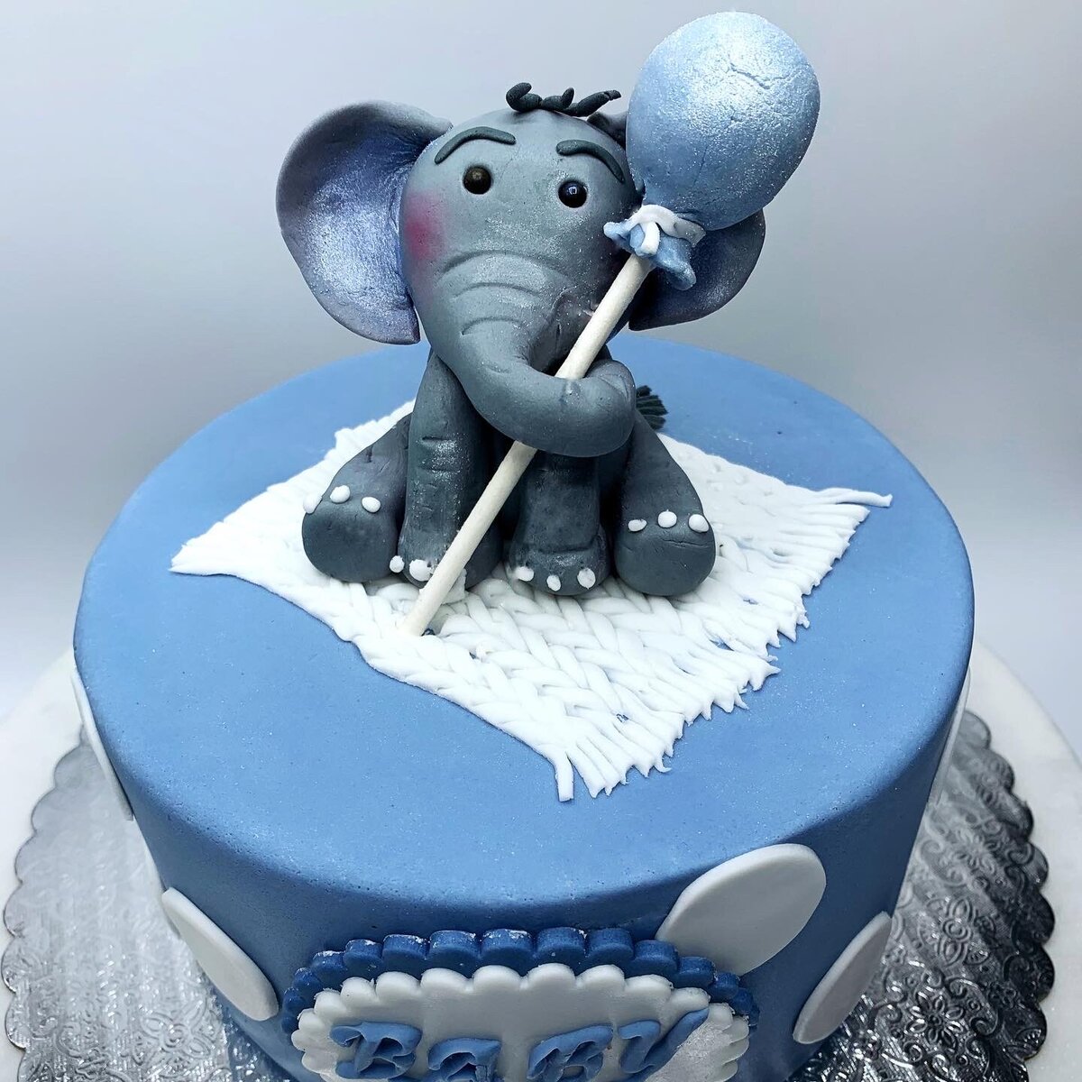 Hand modeled baby elephant holding a blue balloon sitting on top of blue decorated cake