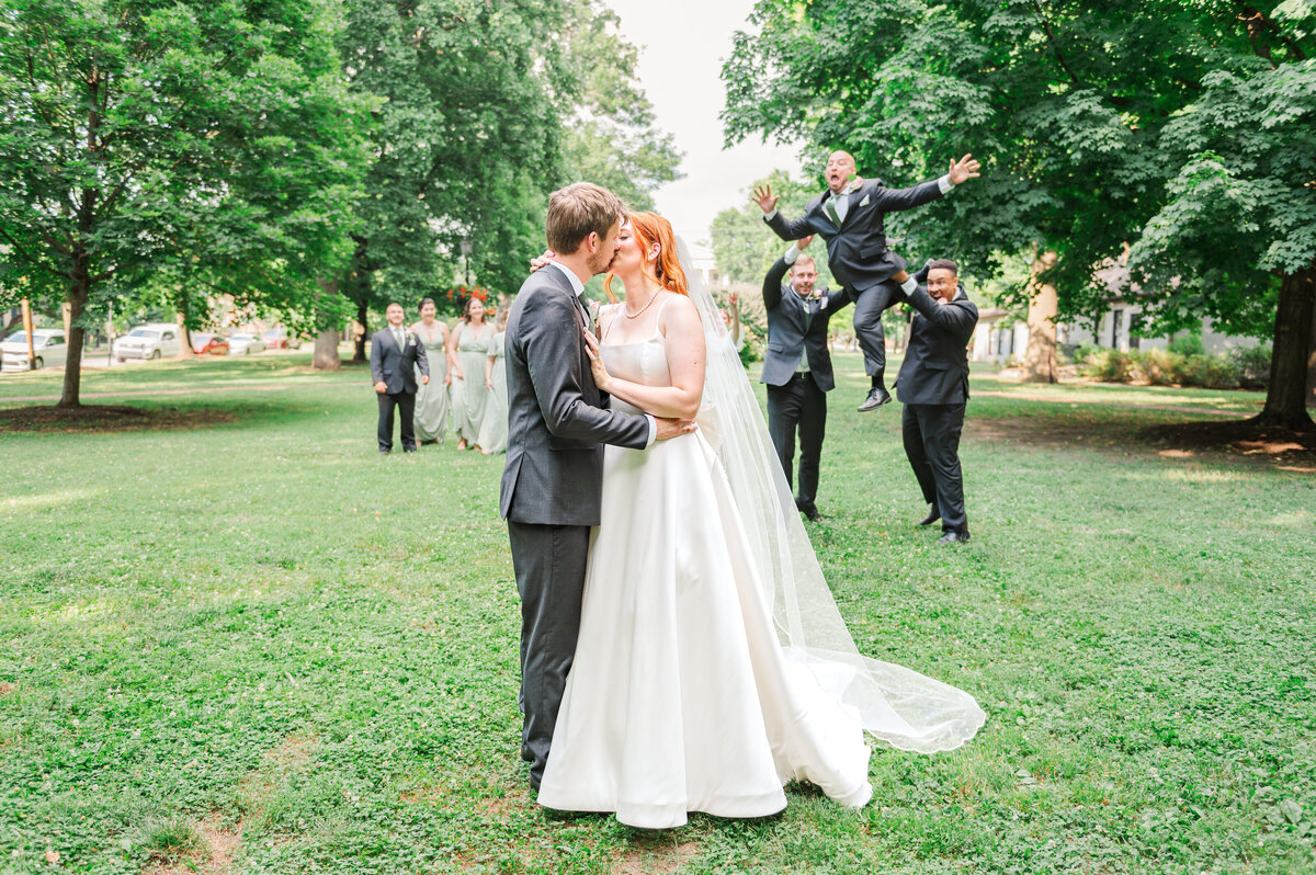 bride and groom kissing while bridal party is having fun in the background