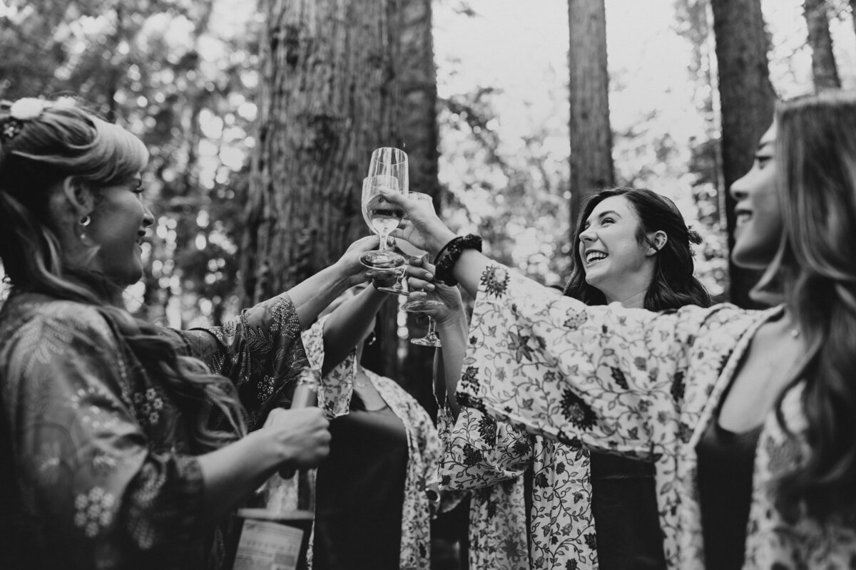 A black and white photo of women toasting with champagne glasses in a forest setting