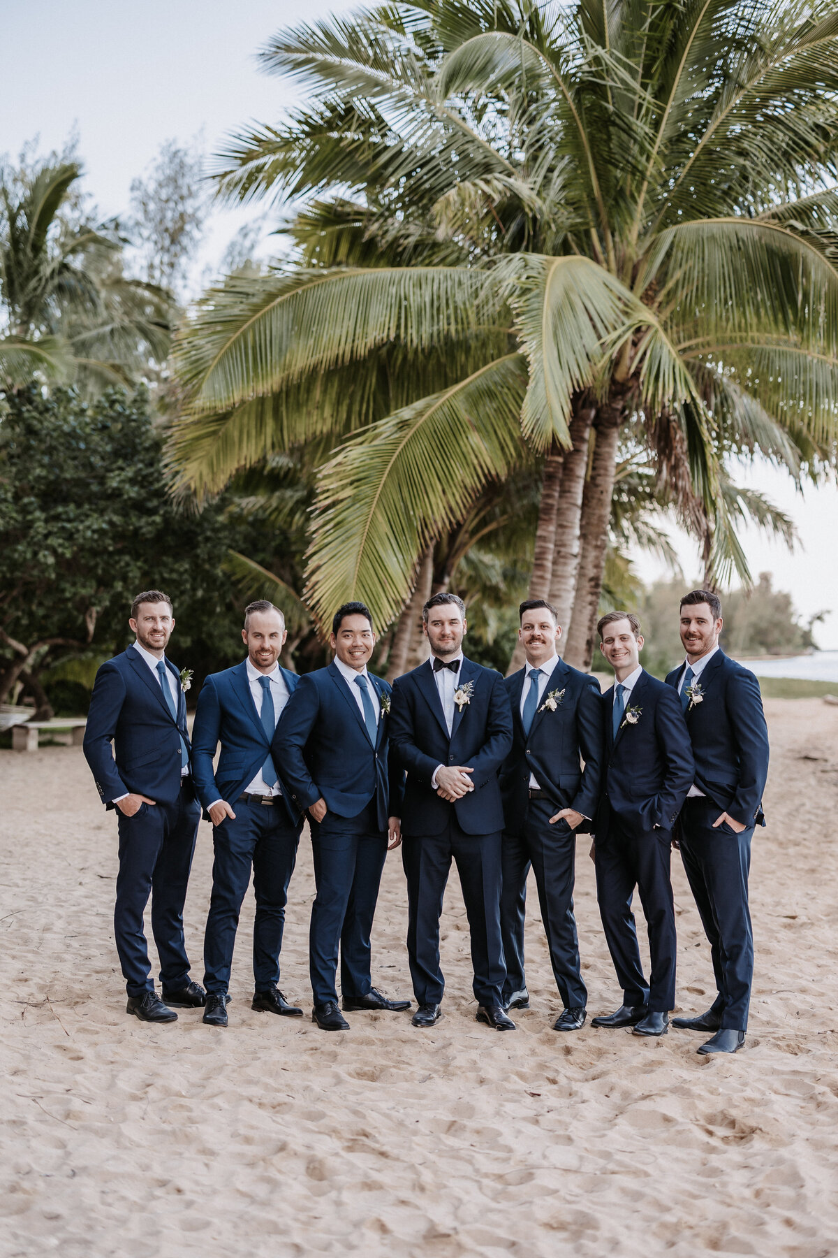 Groomsmen portrait on the beach with palm trees behind wearing navy blue suits