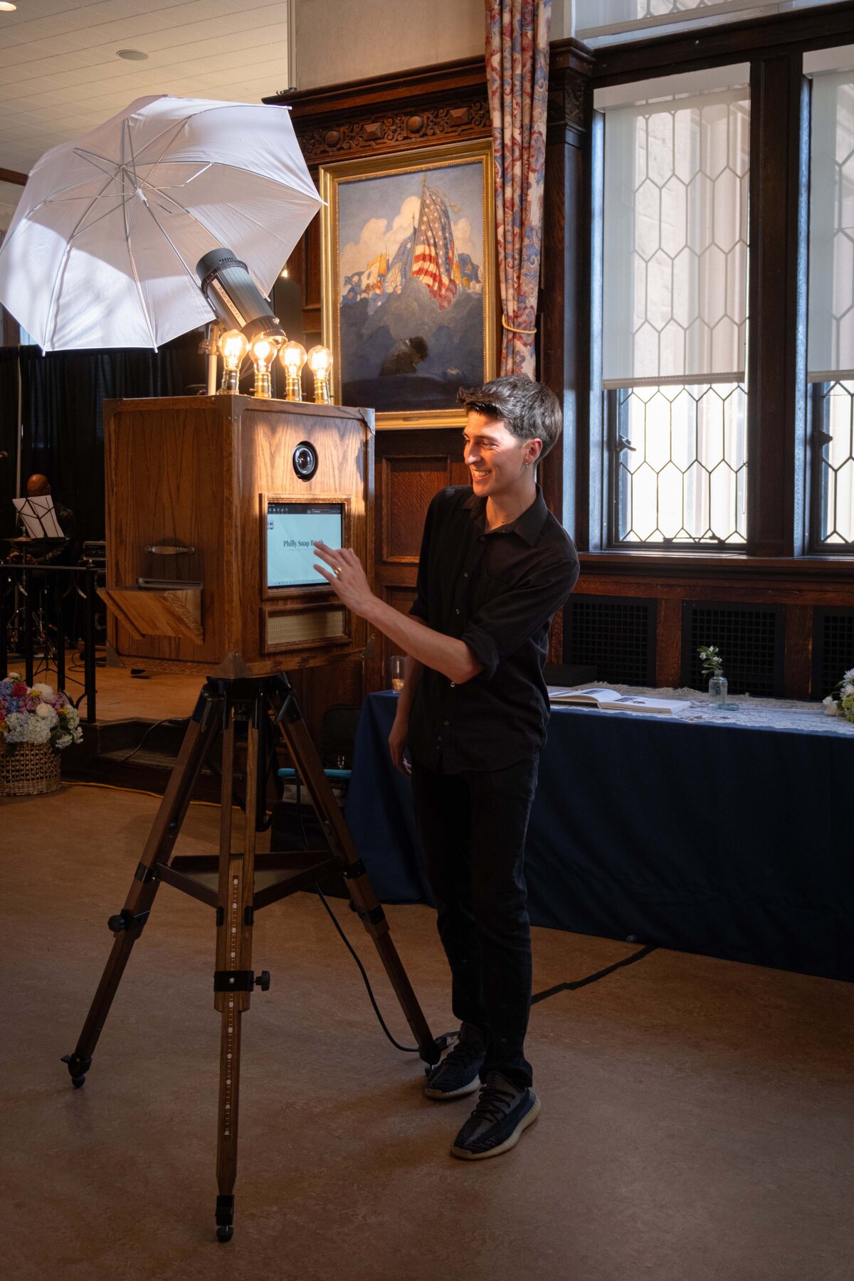 Event attendant preparing a vintage wooden photo booth with umbrella lighting indoors.
