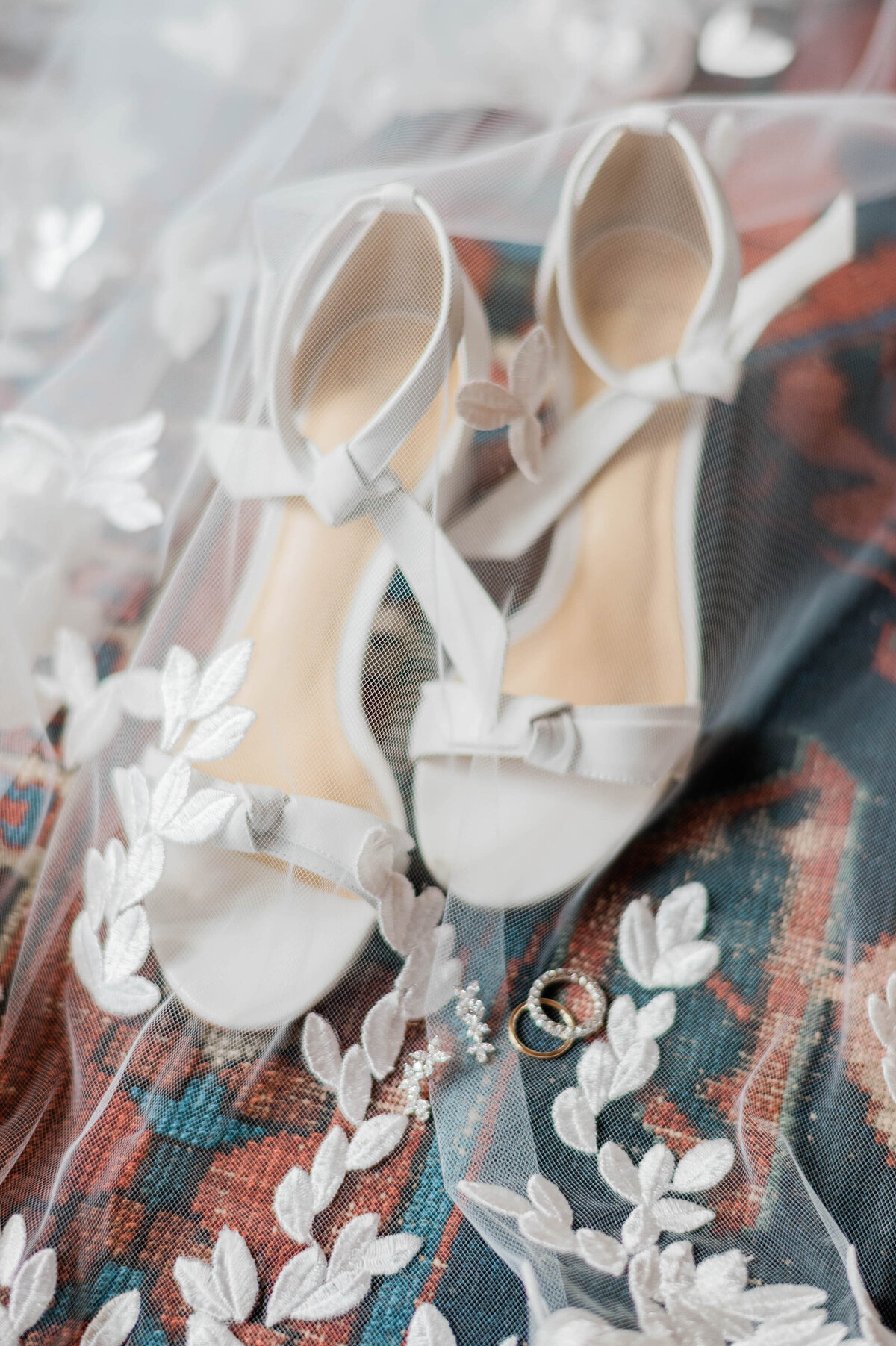 White heels and wedding bands underneath a wedding veil 
