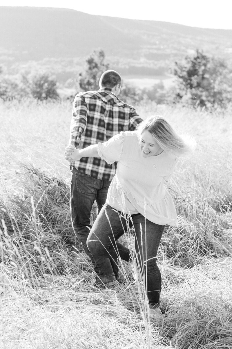 Black and white photo of engaged couple spinning in a field laughing together in Schoharie, NY.