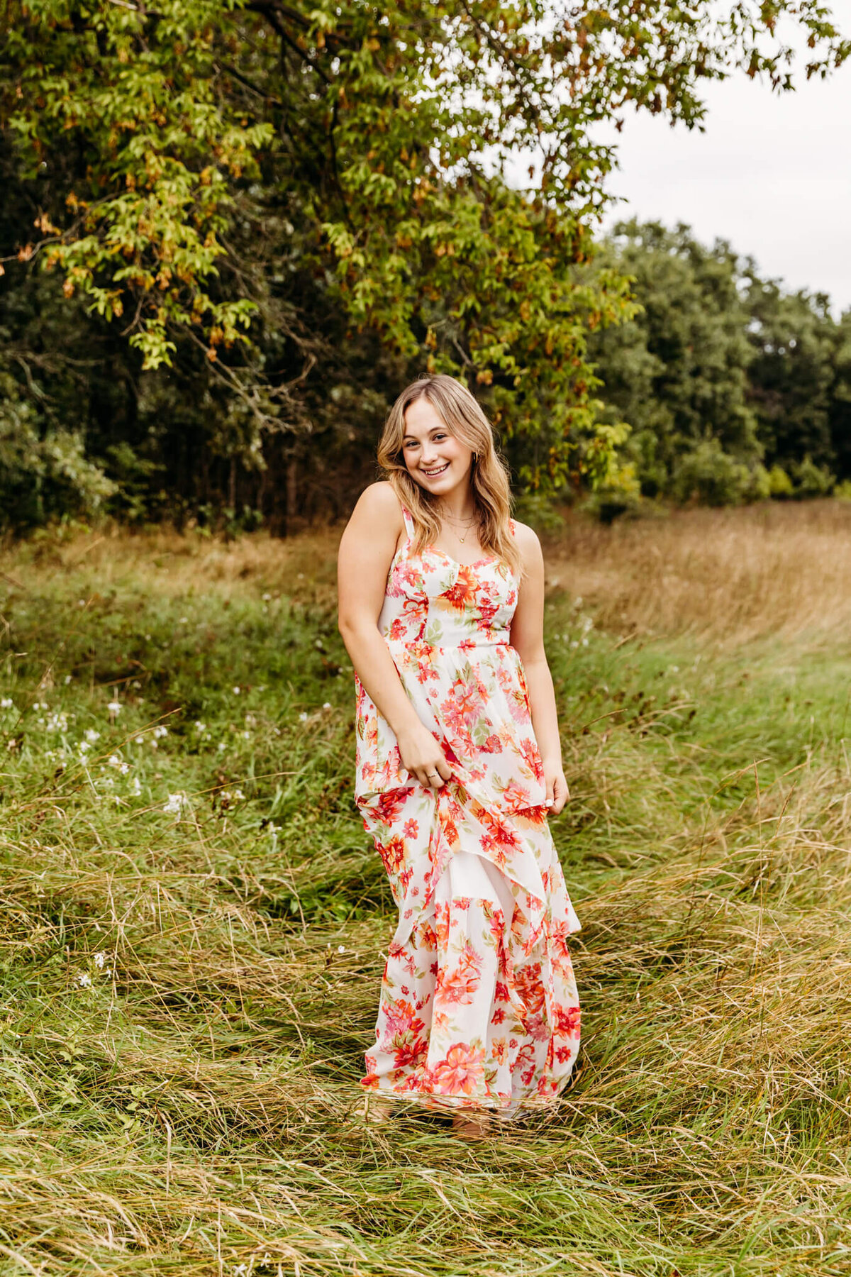 pretty high school girl in a red and pink floral dress playing with her skirt and smiling captured by Ashley Kalbus Photography