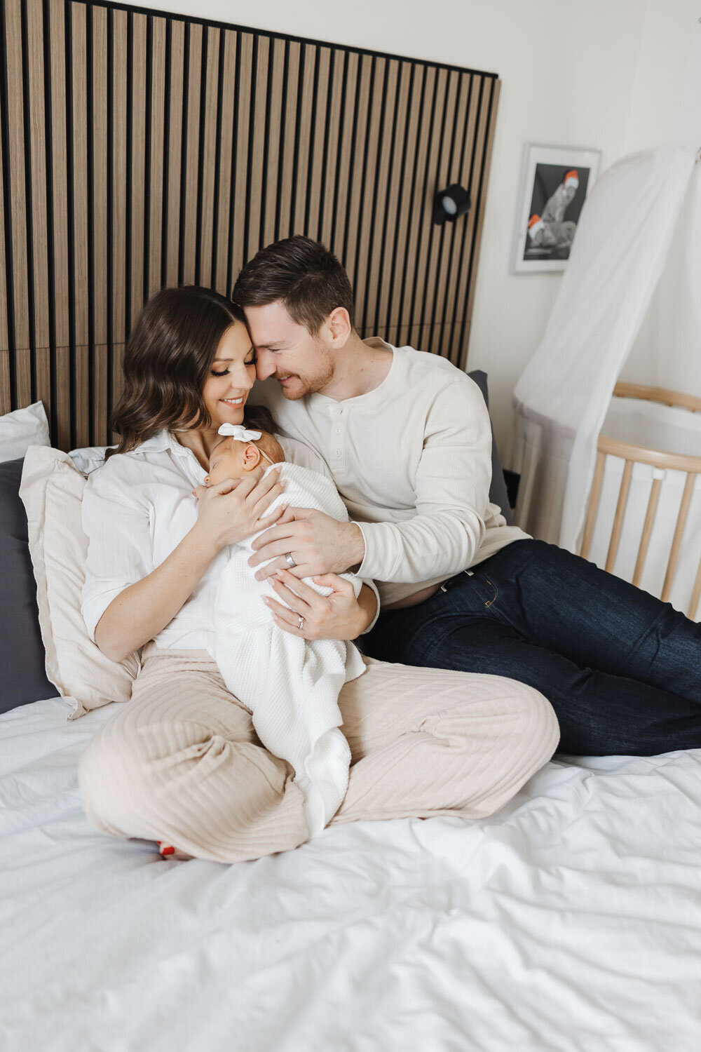 Couple cozy up with their newborn daughter while sitting on their bed in their Toronto Home.