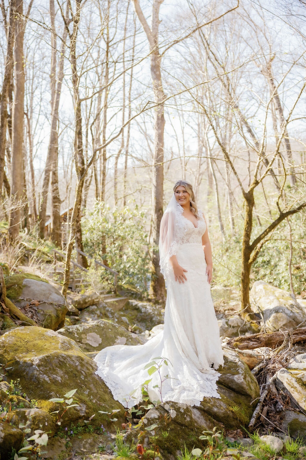 Smoky Mountain elopement photos with bride on a boulder int he forest smiling over her shoulder as the morning sun illuminates her gown