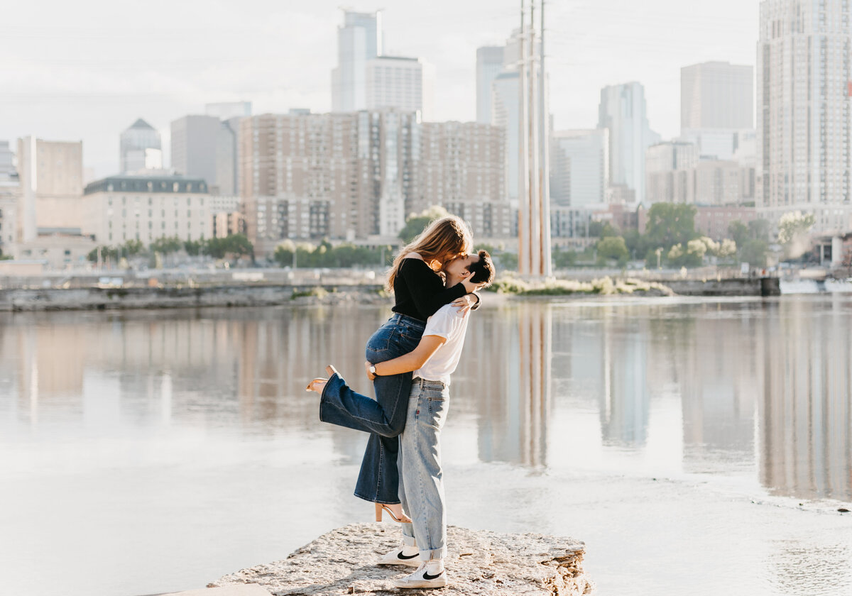 Man picking up woman and kidding her in front of a city skyline and water