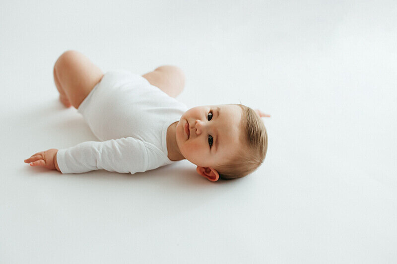 six month old baby boy laying on his back on white backdrop