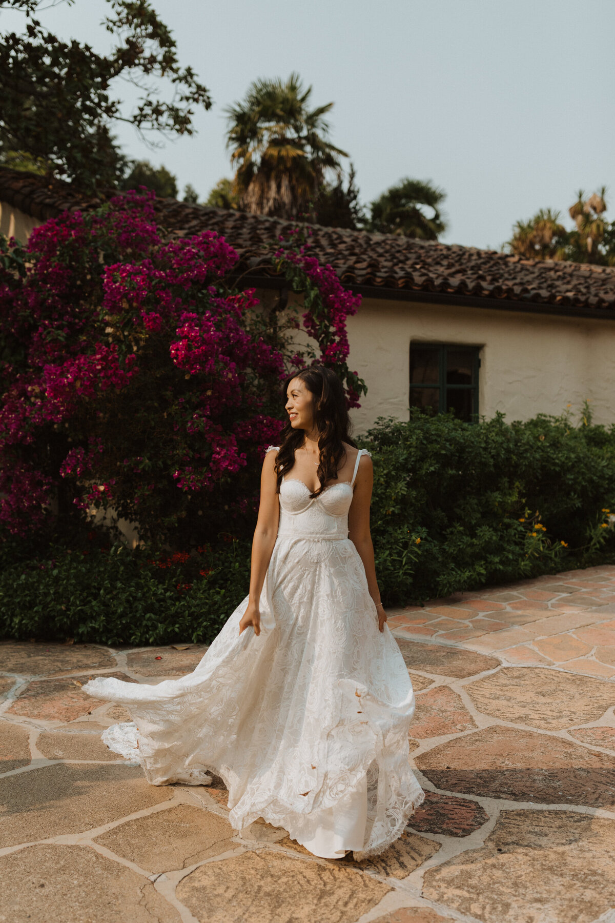 Bride with wedding dress blowing in the wind standing in front of Pueblo style building and pink bushes
