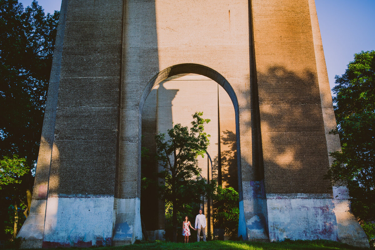 A couple standing under the hell gate bridge in astoria park nyc during their engagement session