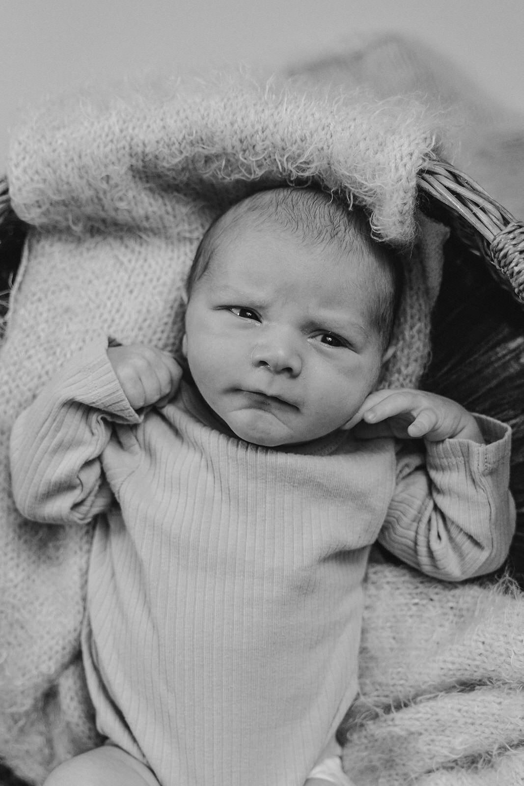 A newborn laying down with their hands by their face