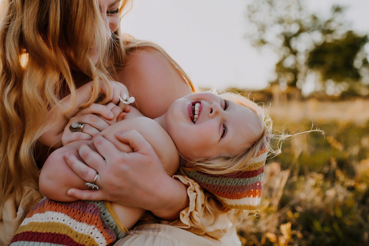 A mom and daughter sitting on the ground in flower mound, texas giggling with one another
