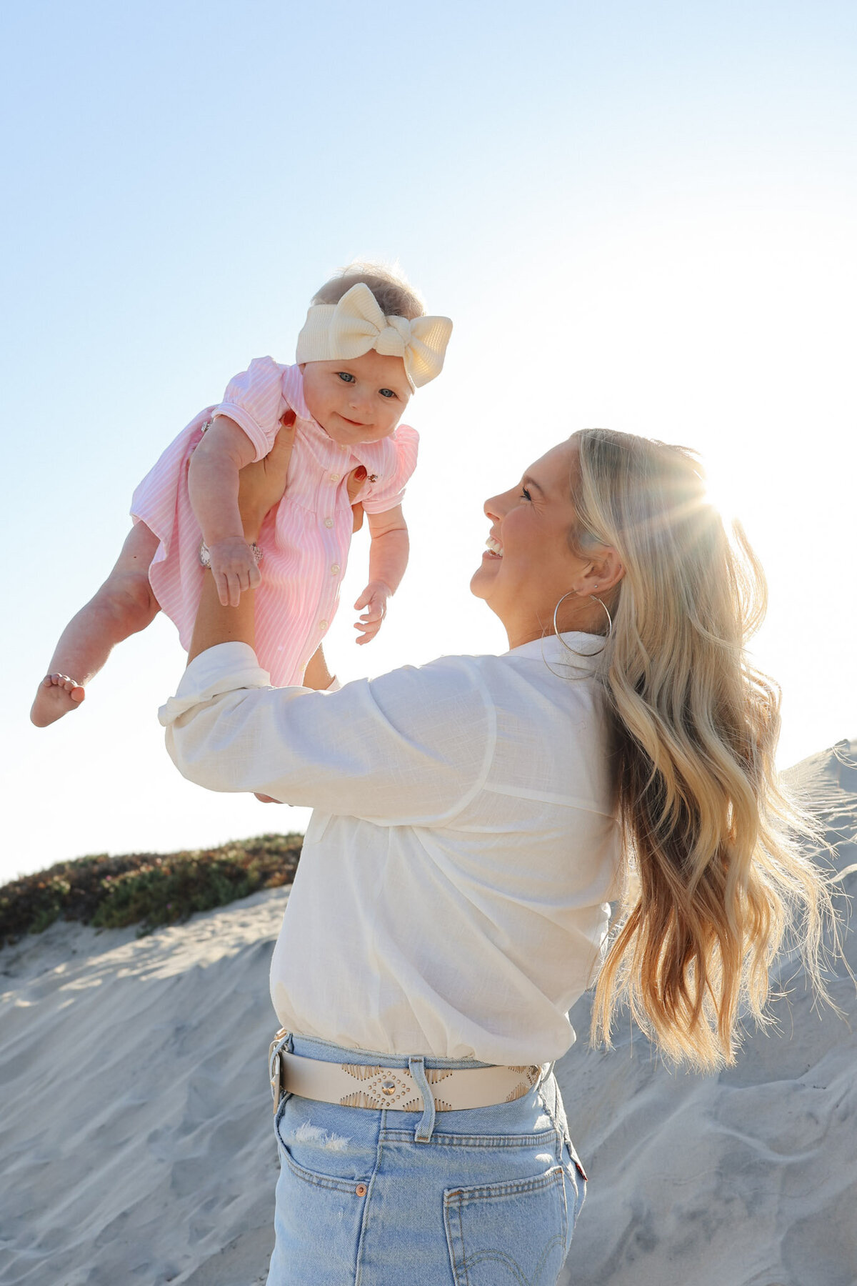 A woman and a child joyfully playing together on the beach, captured by a family photographer.