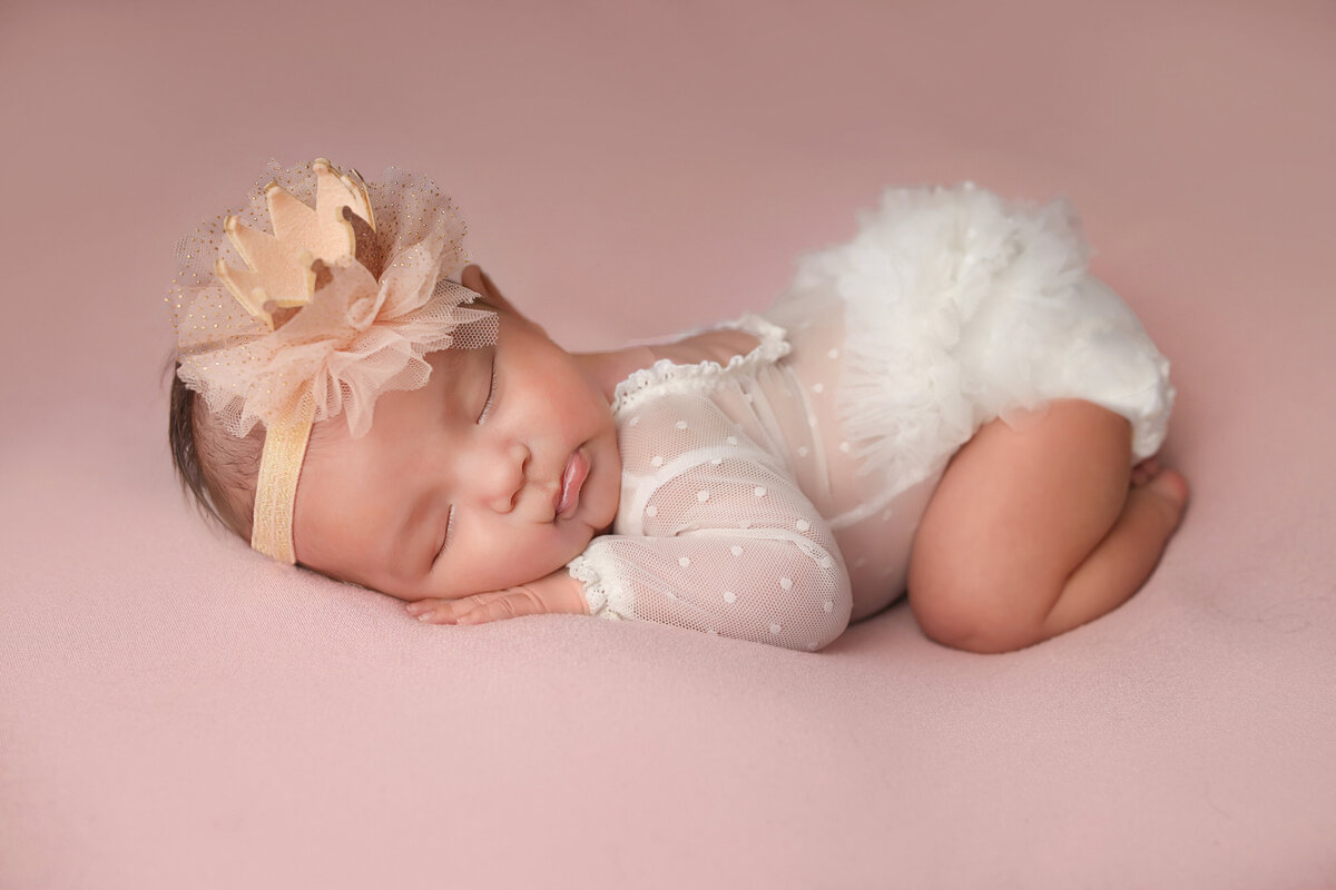 Sleeping newborn in white lace laying on vintage wooden bed.
