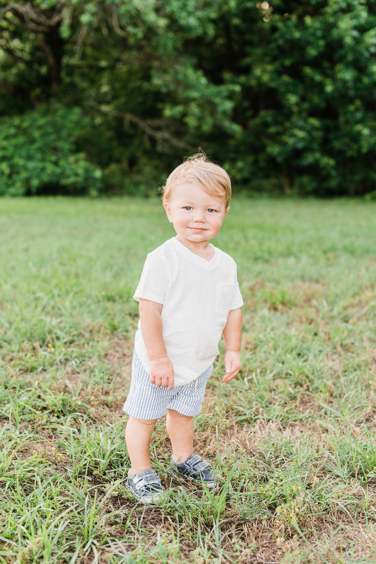 Toddler in white shirt and blue shorts pauses for a photo during a family session in Raleigh NC. Photographed by Raleigh NC family photographer A.J. Dunlap Photography.