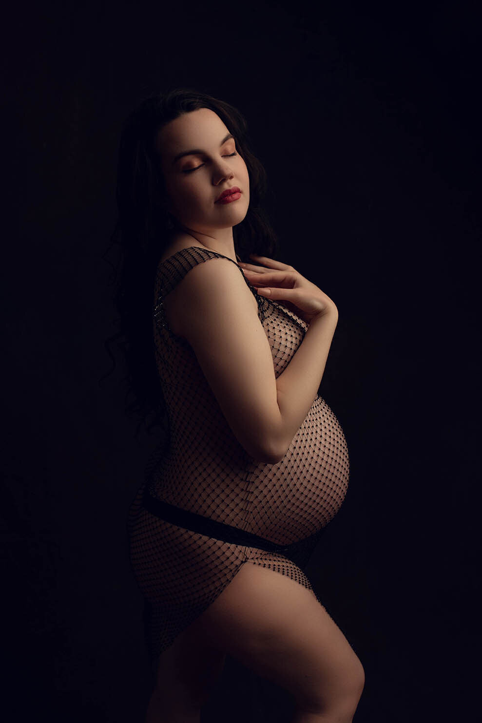 a dramatically lit photo of a pregnant woman wearing a rhinestone dress with nothing underneath