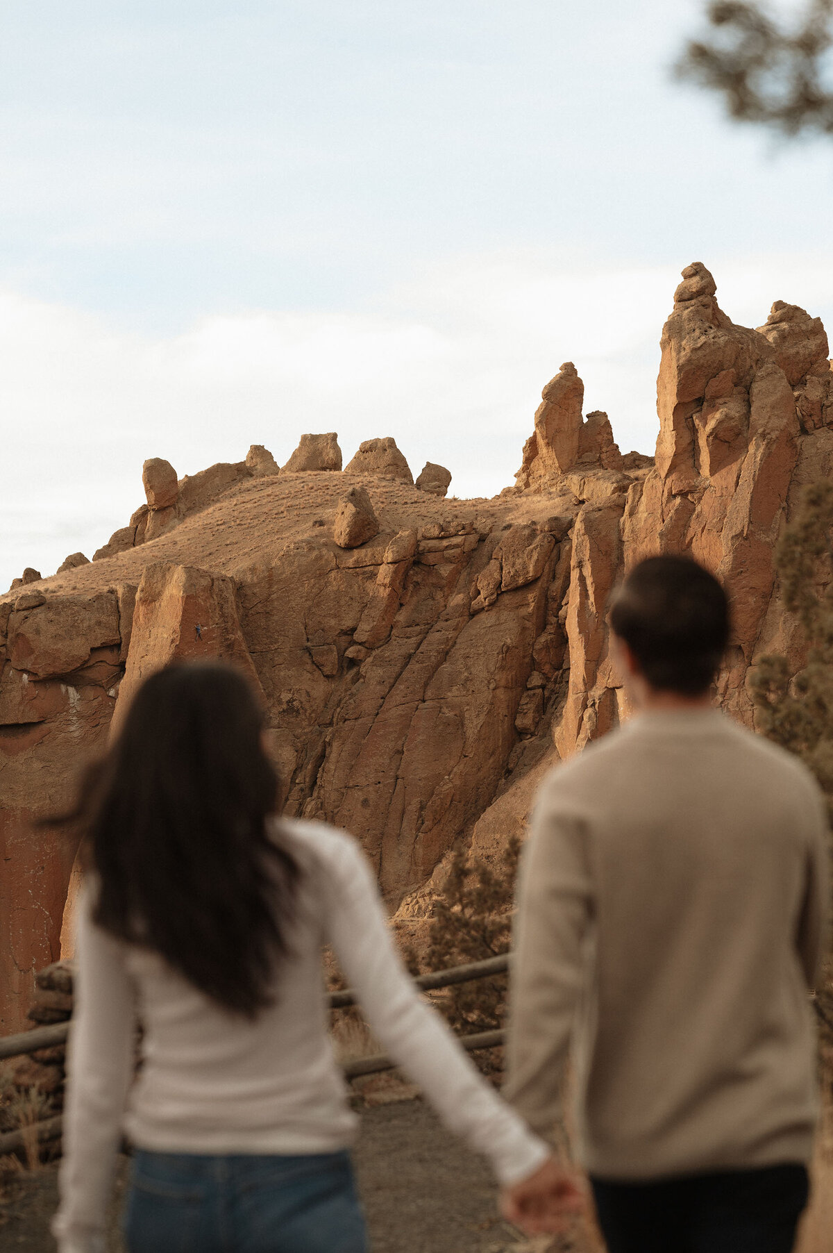 engaged couple holds hands and stands in front of jagged rocks at Smith Rock State Park in Bend, Oregon