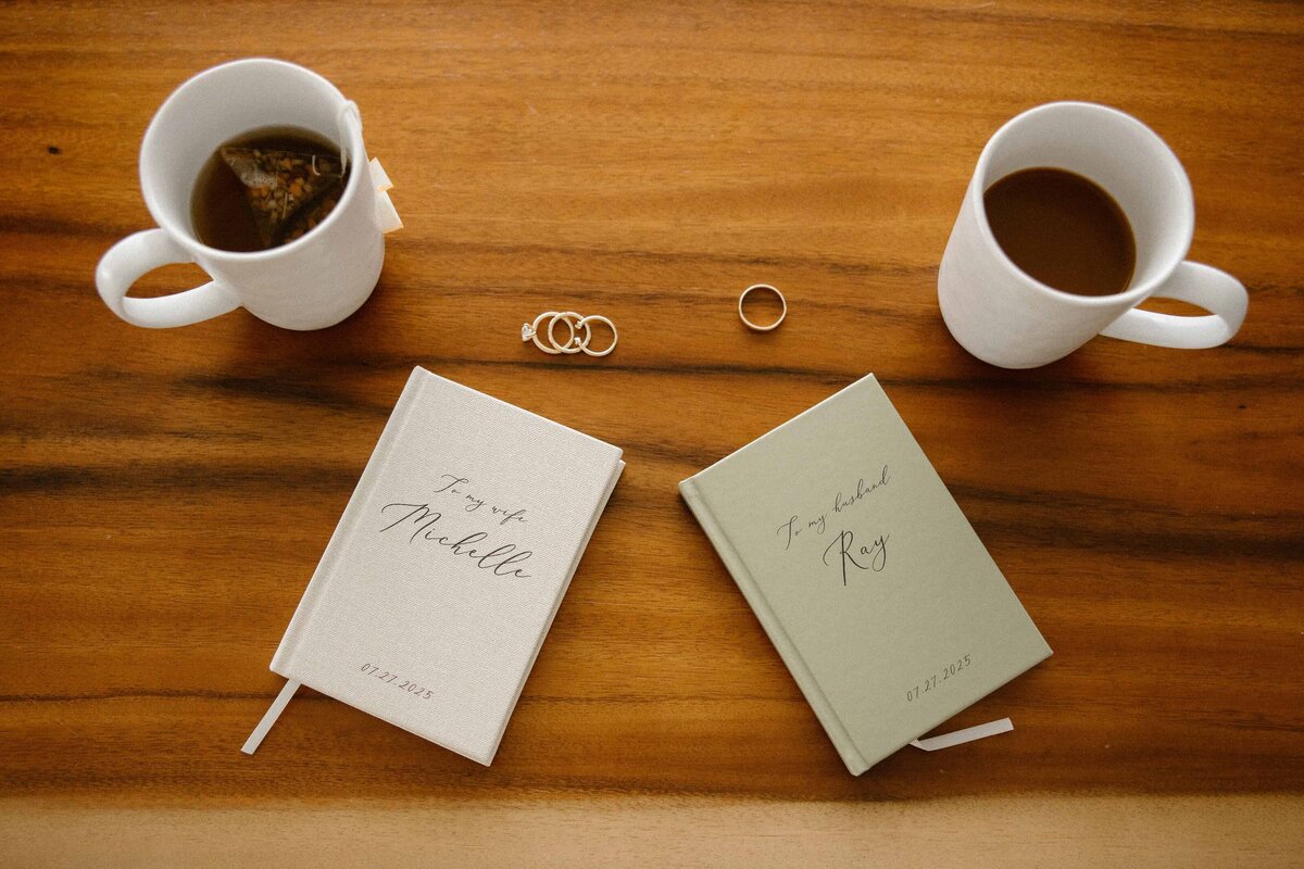A pair of vow books, coffee cups and wedding rings lay on a table before a Colorado Elopement.