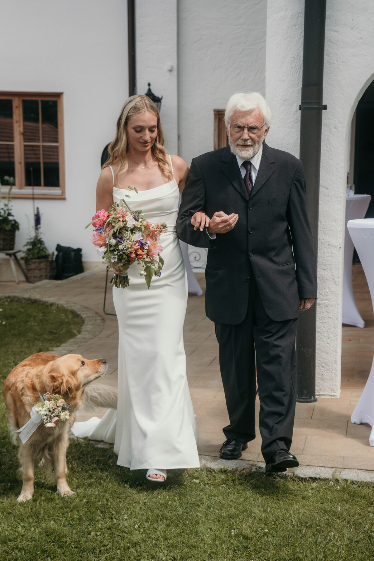The father of the bride guides his daughter to the free wedding ceremony, accompanied by their dog.