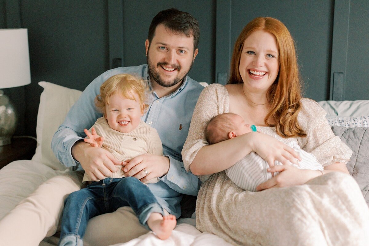 family-of-four-lauging-at-camera-on-bed