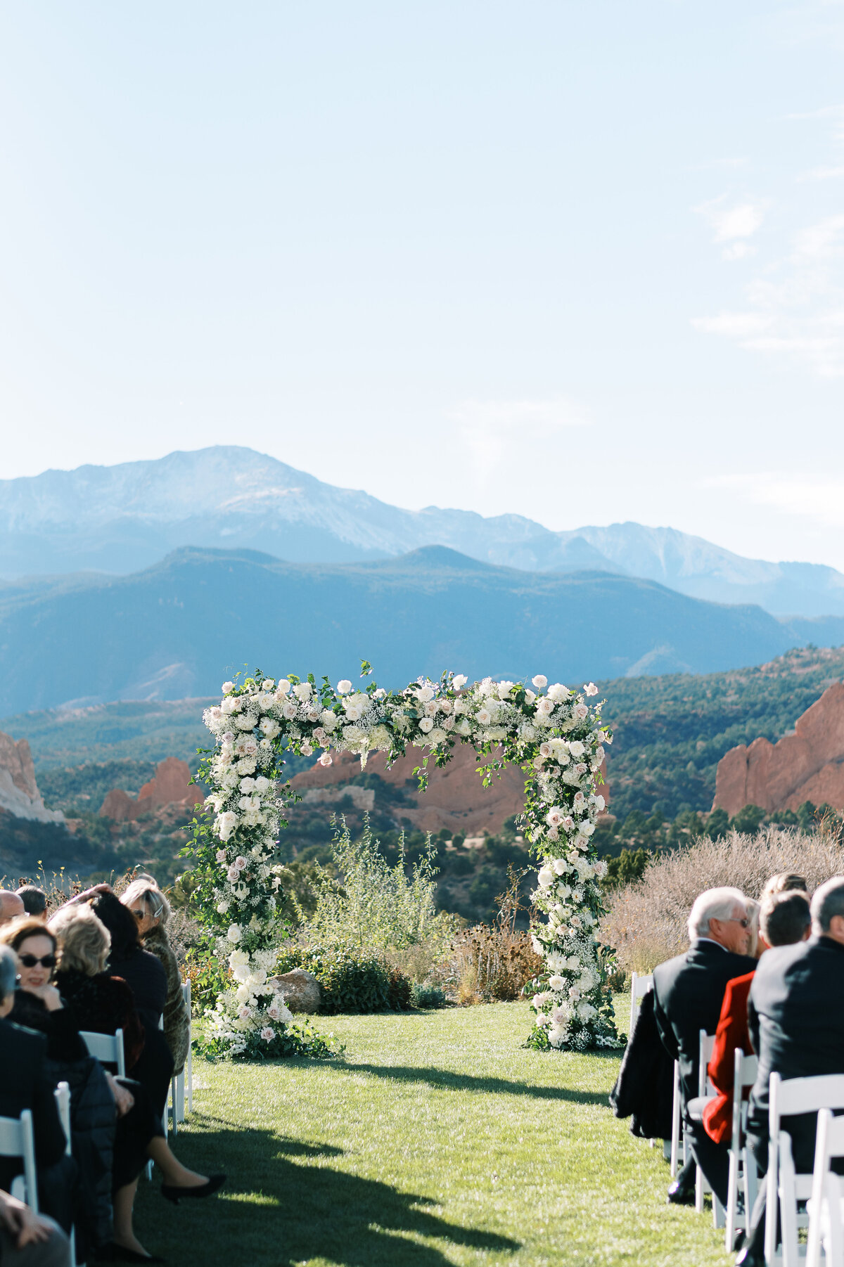 Garden of the Gods country club in Colorado Springs with a white floral arch for a wedding ceremony with guests by Colorado Wedding Photographer JKG Photography
