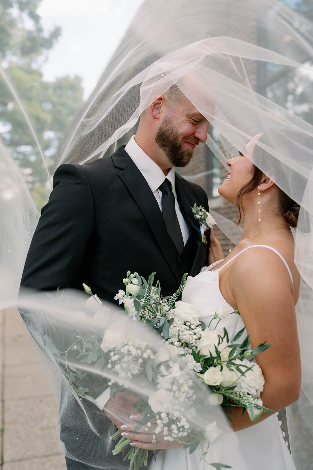 Bride and groom looking at each other while wrapped in the bride’s veil at their Leona Road wedding in Grand Rapids MI, creating a romantic golden hour moment.