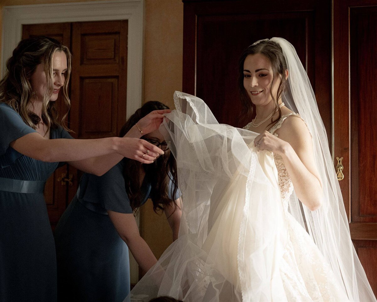Final preparations as two bridesmaids adjust a brides dress.